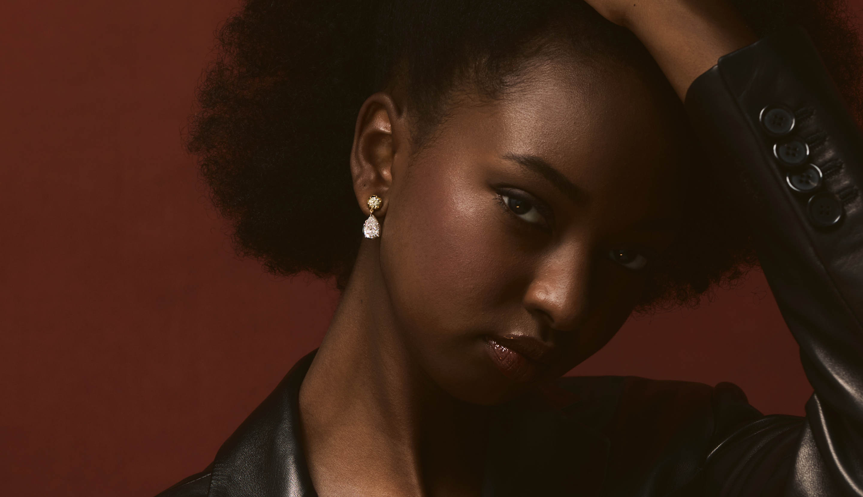 Blonde woman with slicked-back hair wearing a black strapless top and a choker necklace with a large light blue gemstone.