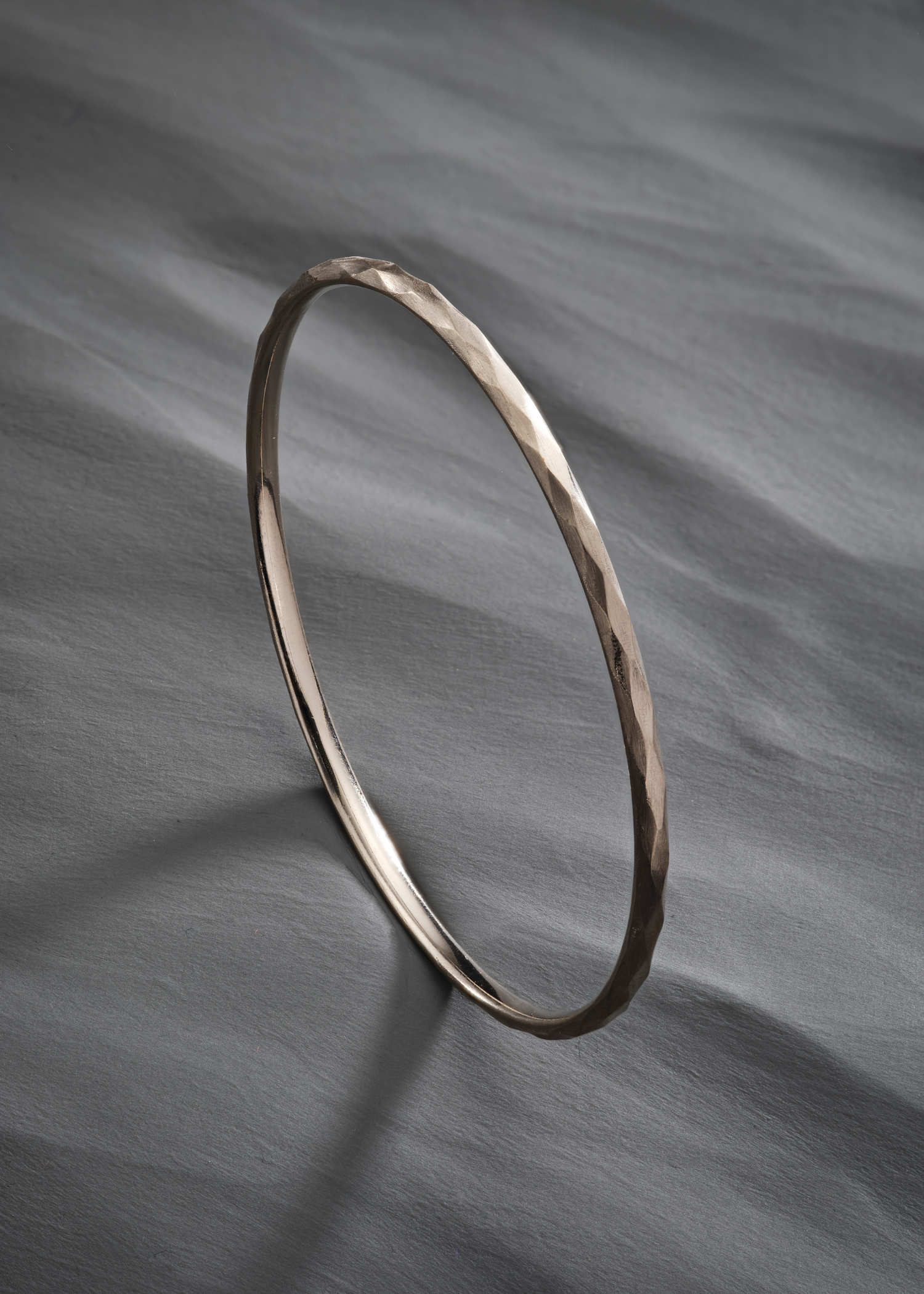 White gold faceted bangle with a subtle hammered texture on a white background.