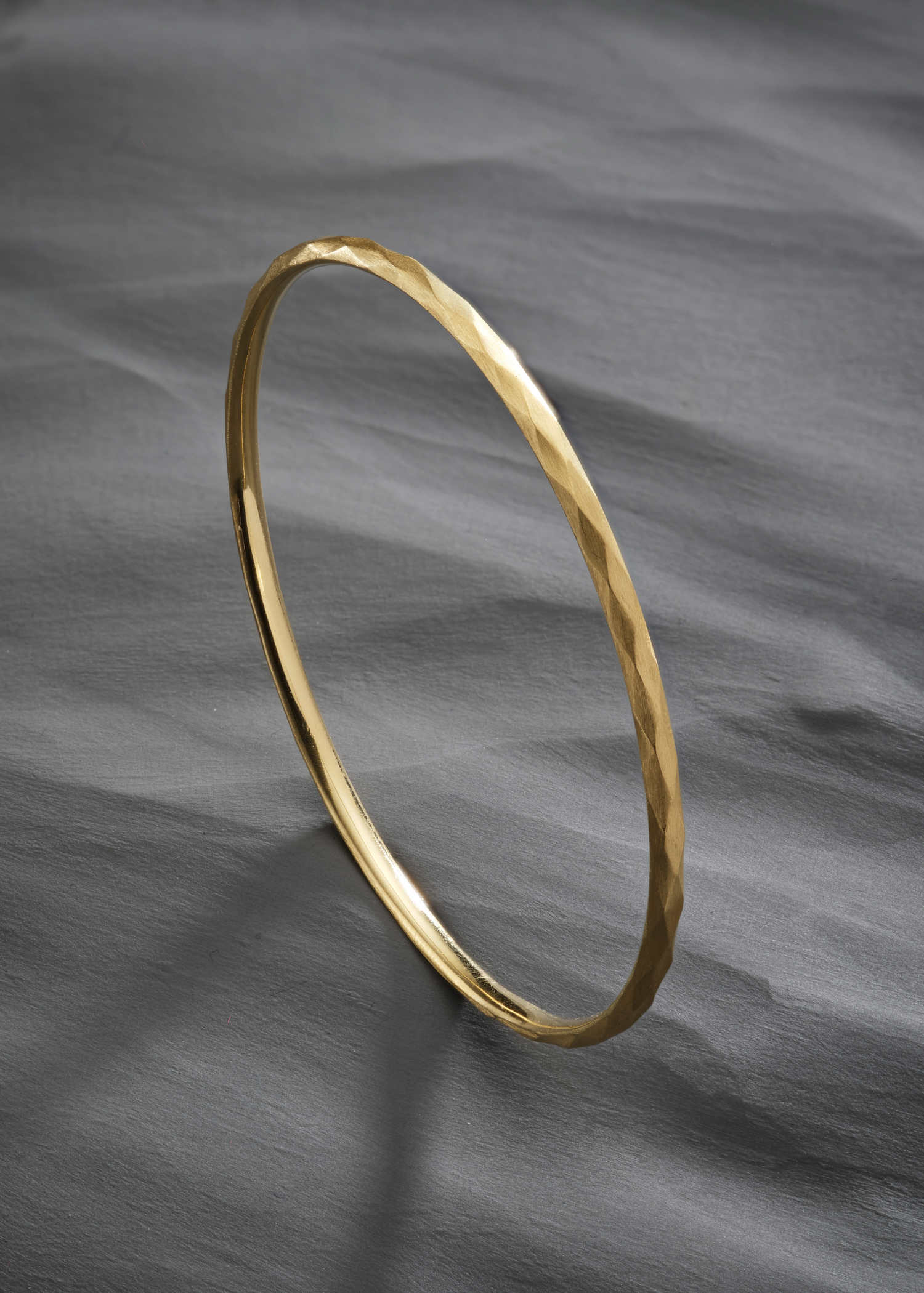 White gold faceted bangle with a subtle hammered texture on a white background.