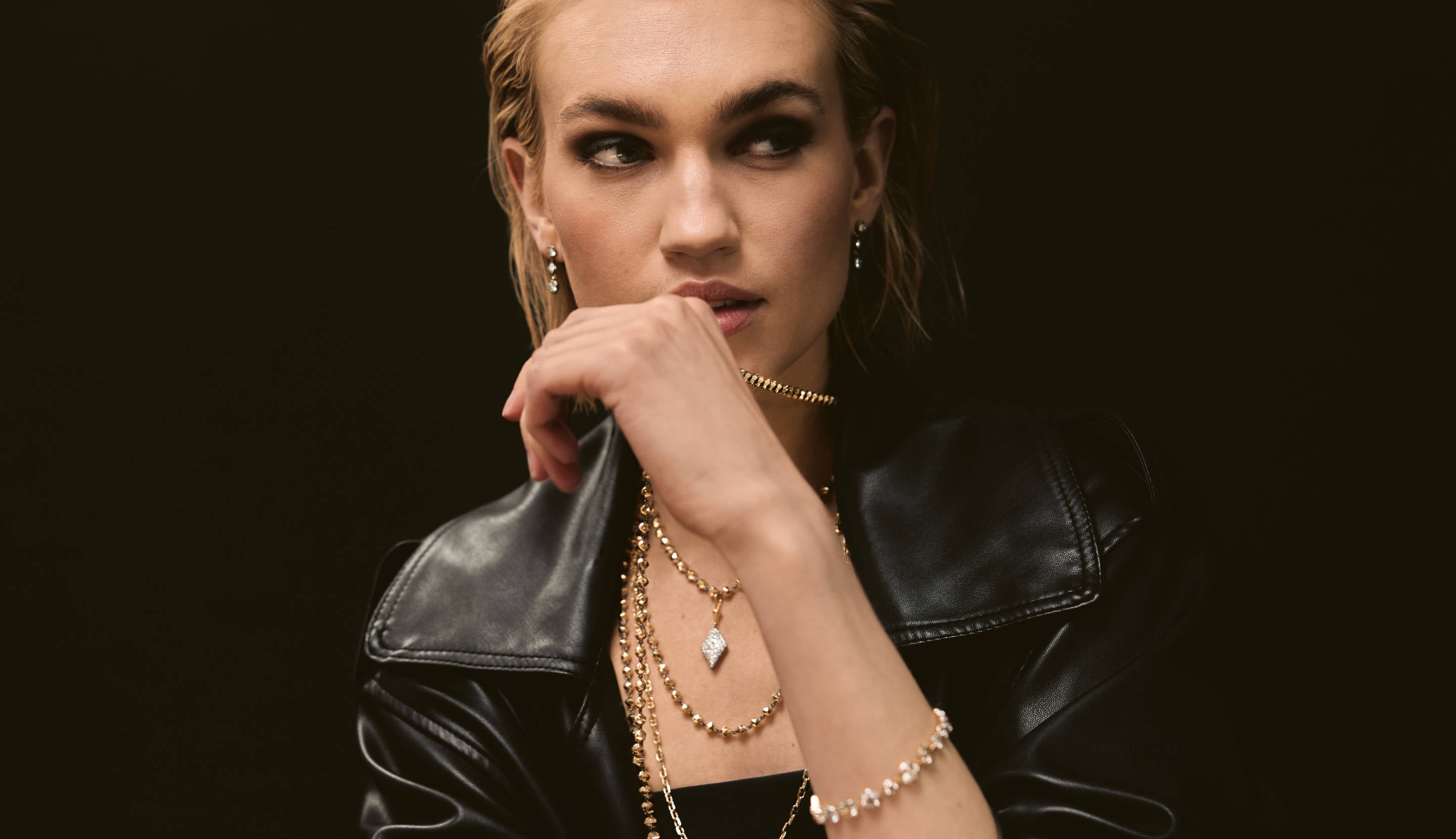 Blonde woman with slicked-back hair wearing a black strapless top and a choker necklace with a large light blue gemstone.