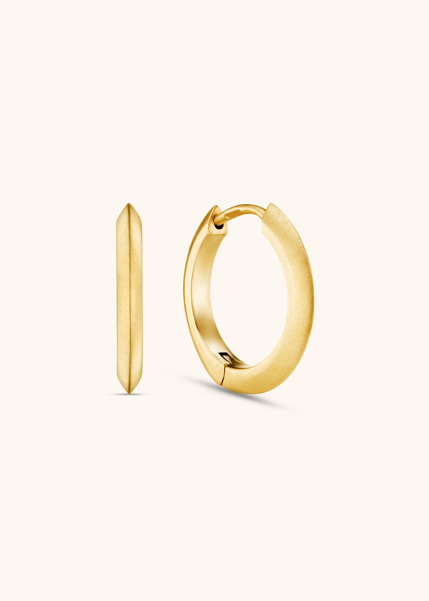 Brushed 18k yellow gold oval hoop earrings on textured grey background.