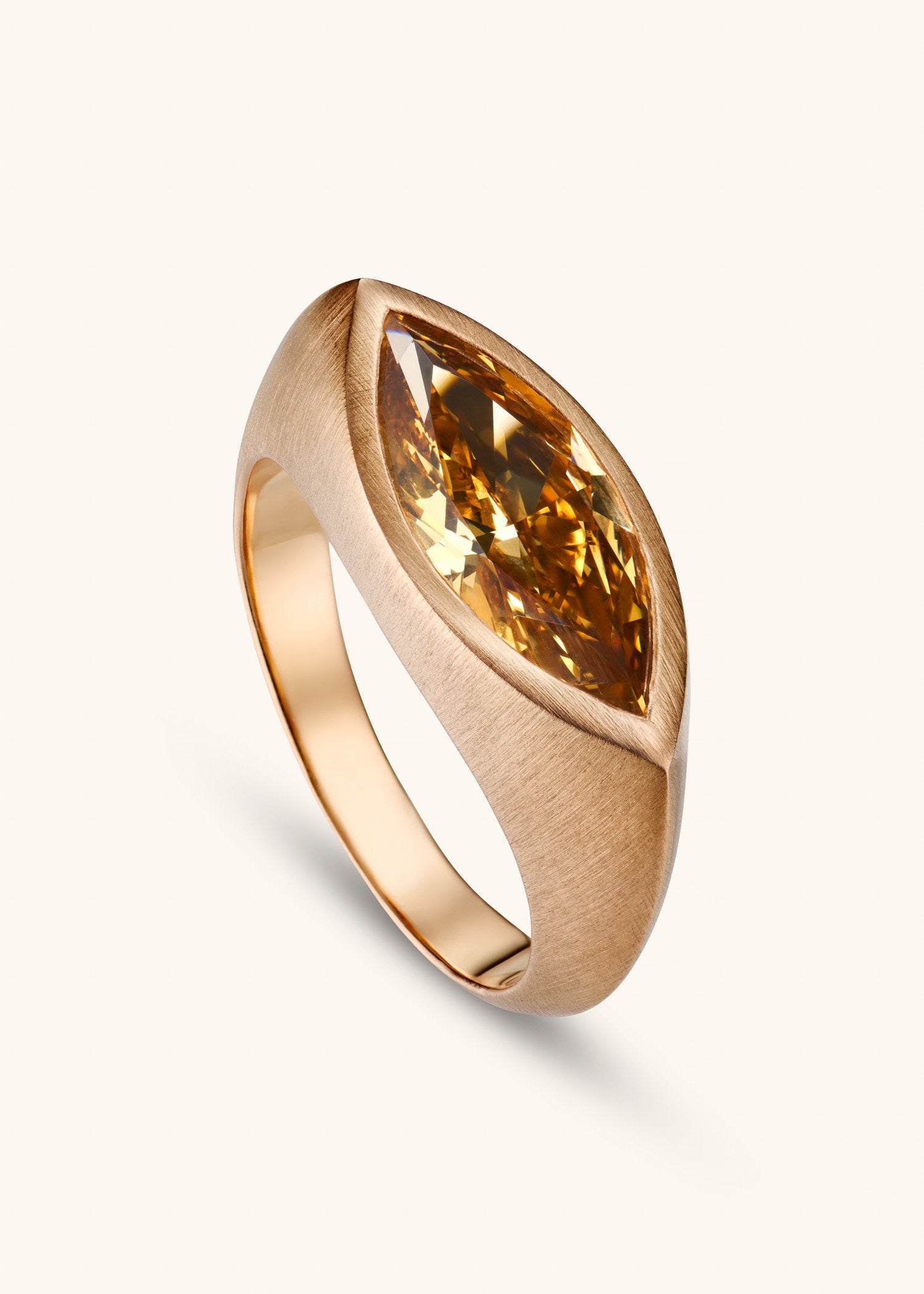 Rose gold ring with a amber stone on a textured beige surface.
