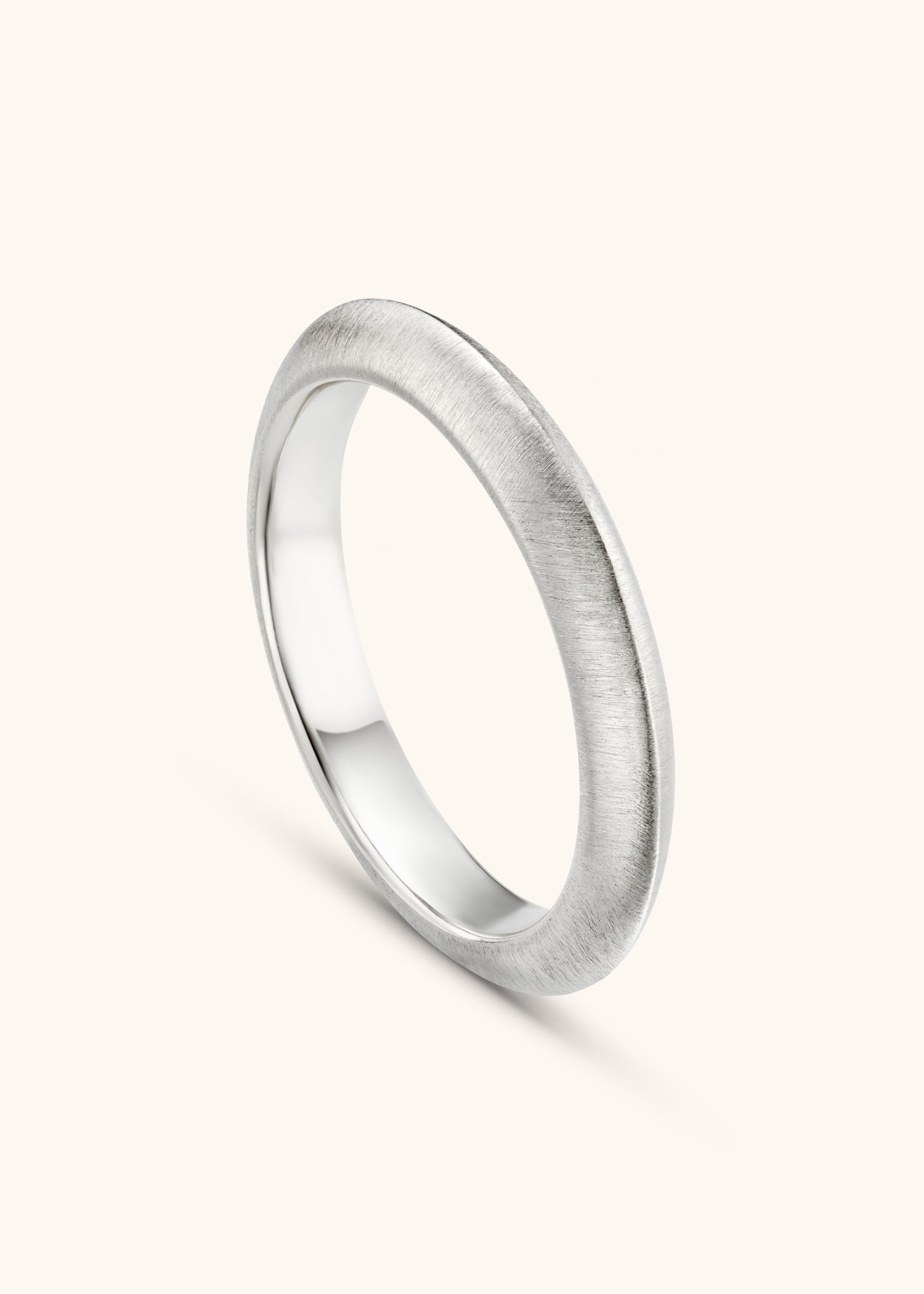 Simple white gold knife-edge ring on a textured gray surface.