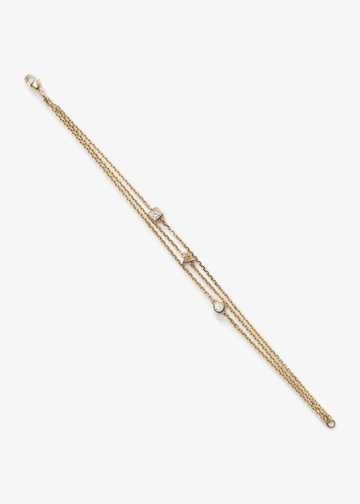 Delicate gold three-strand bracelet featuring round, triangle, and square-cut diamonds, photographed on a textured gray surface.