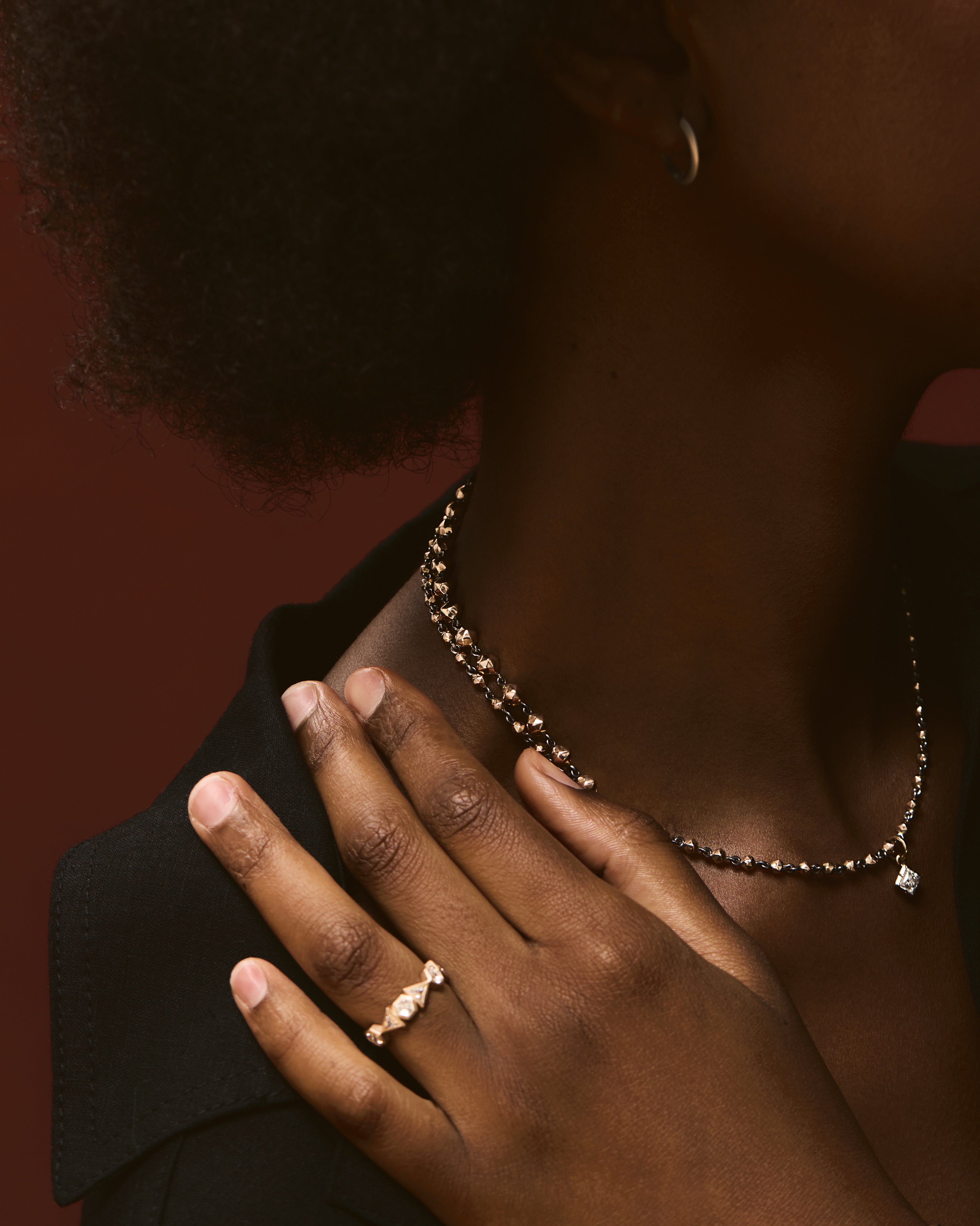 Close-up of a person wearing a necklace and ring with a dark background.