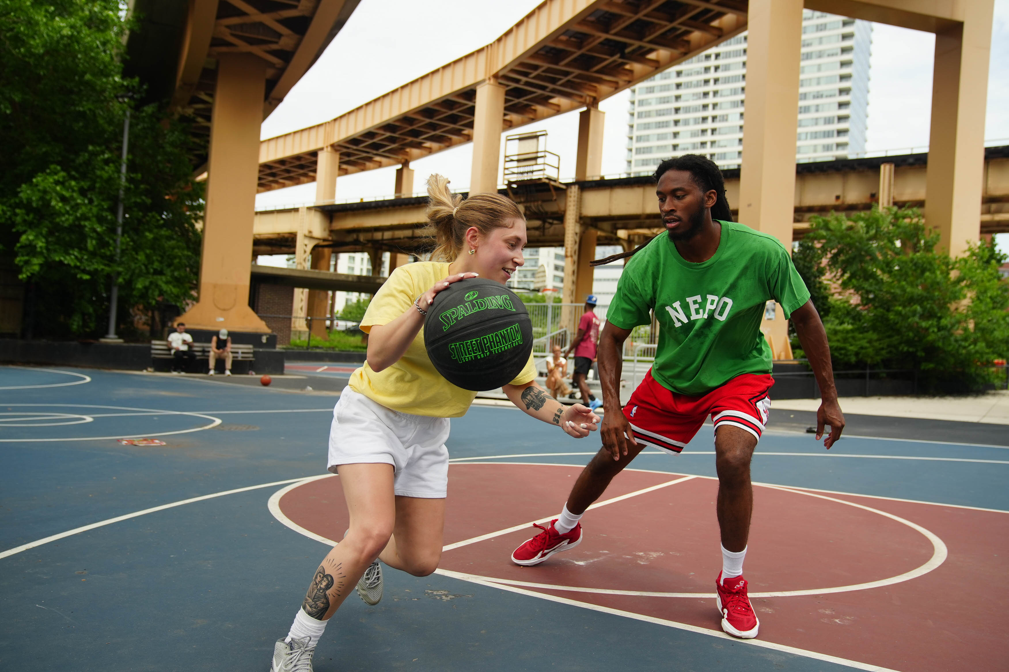 A young man and woman play basketball on an outside court.