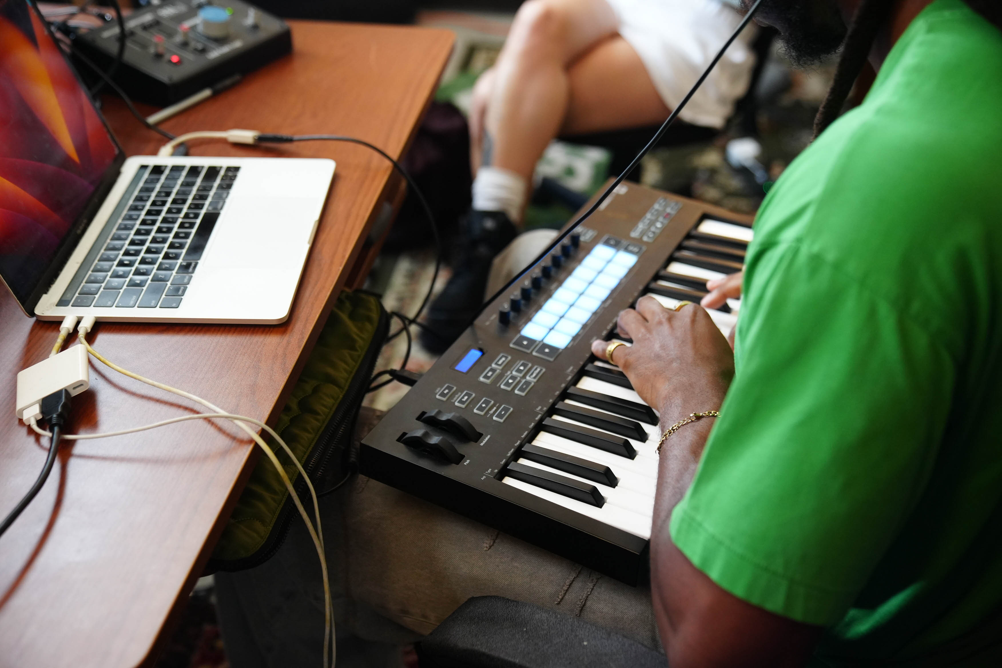 A young man plays a digital keyboard, wires hooking up several instruments and the headphones he wears. 