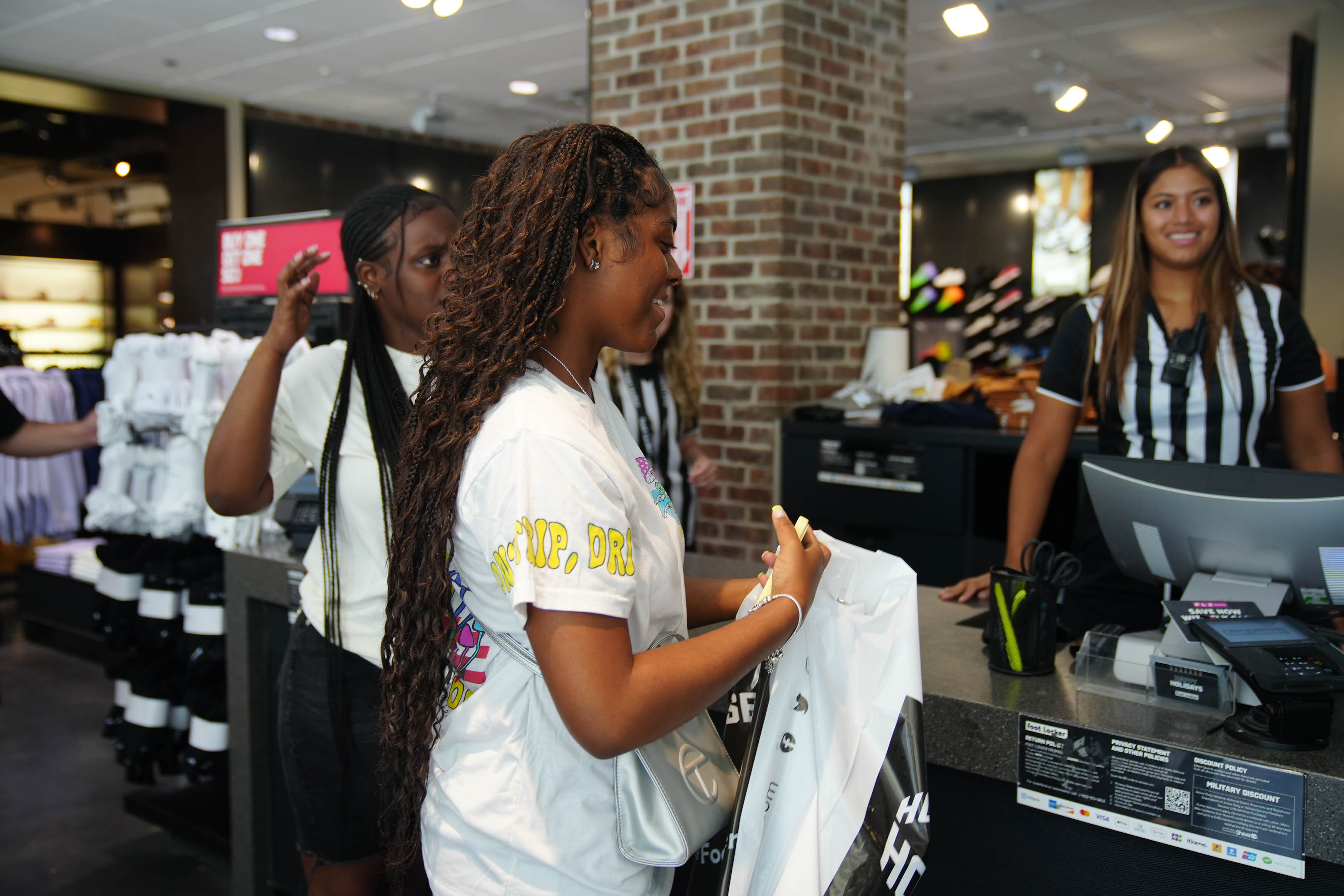 A young woman is holding a shirt at the register in a store.