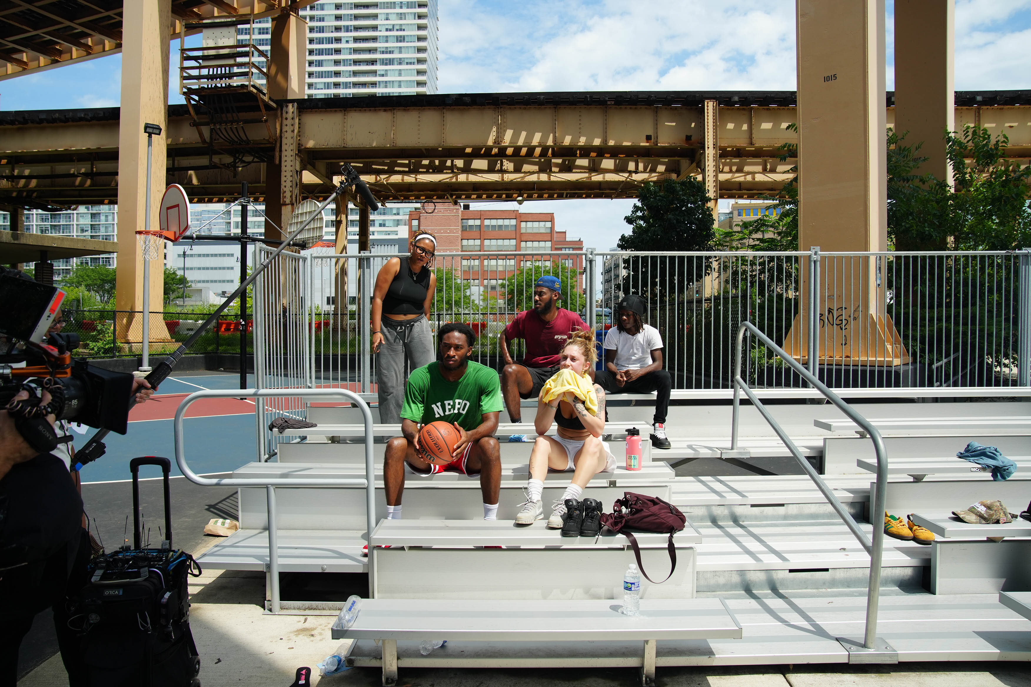 5 teenagers sit on bleachers wearing athletic wear, looking at the camera and mic equipment pointing at them.