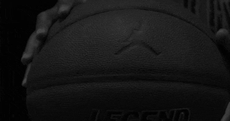 A short clip of a young boy dribbling a basketball while he walks down a sidewalk framed by metal scaffolding.