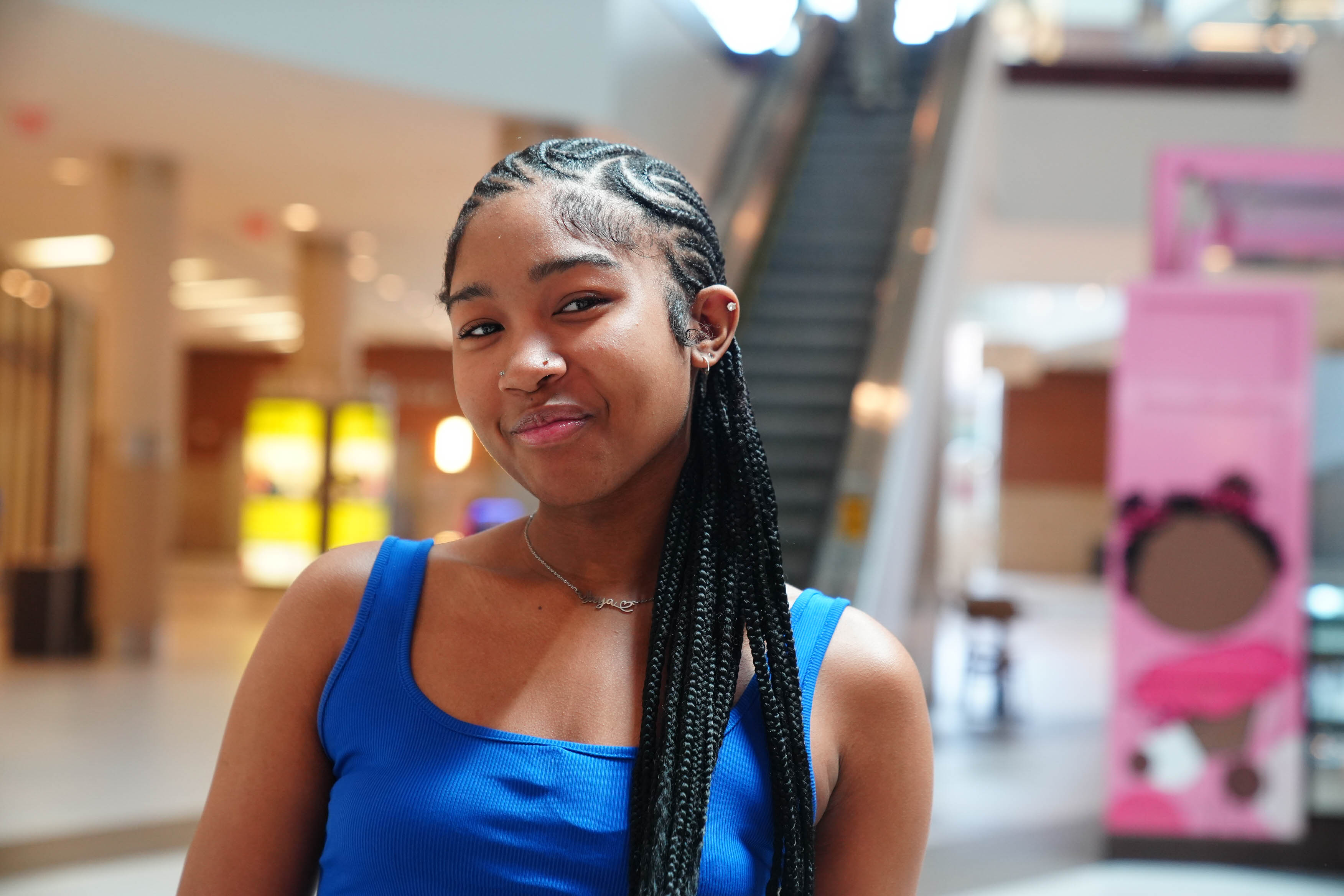A young woman in a mall, wearing a blue tanktop with long cornrows.
