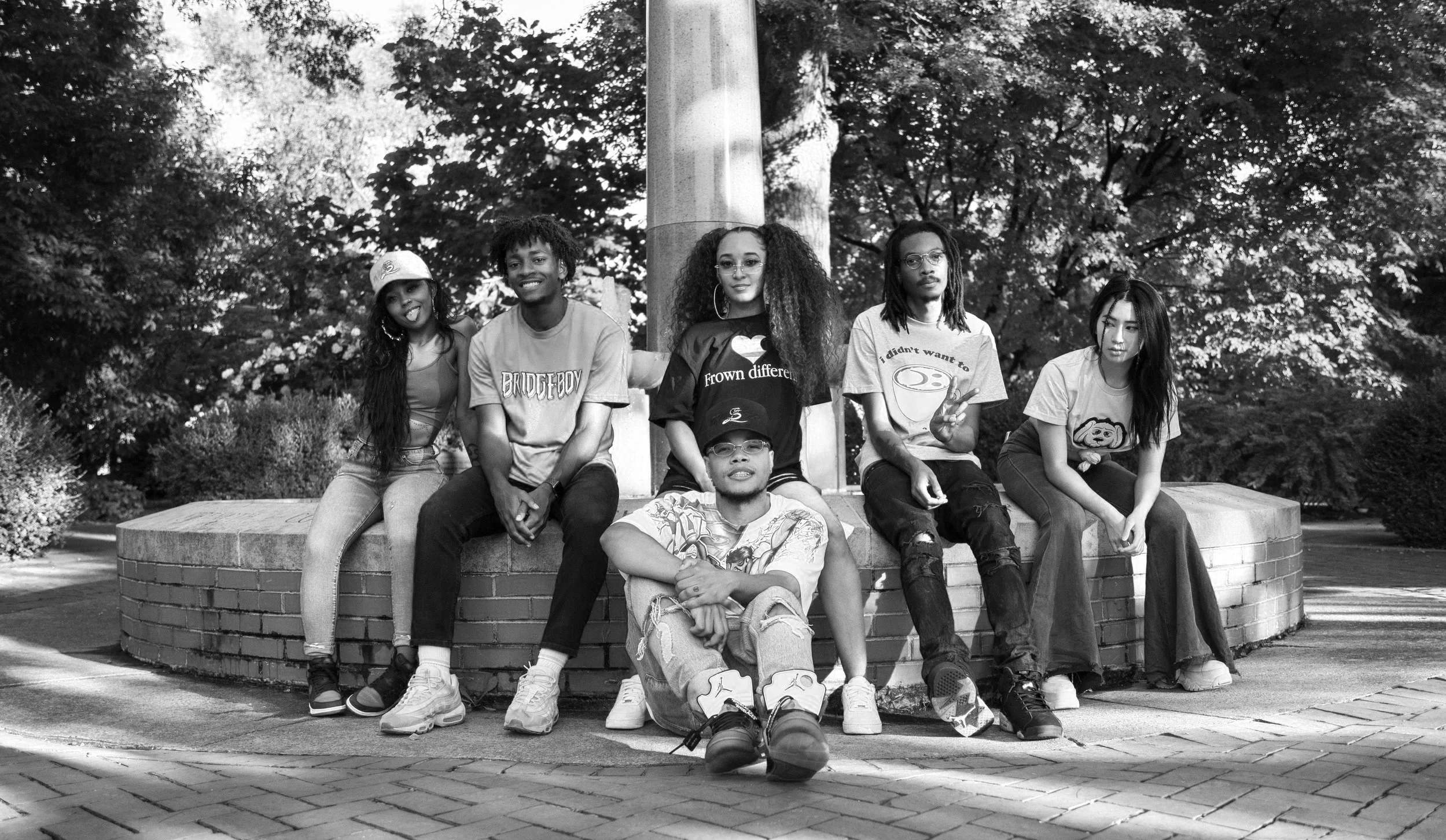 A group of 6 teenagers with different cultural backgrounds, sitting together with serious or smiling faces.