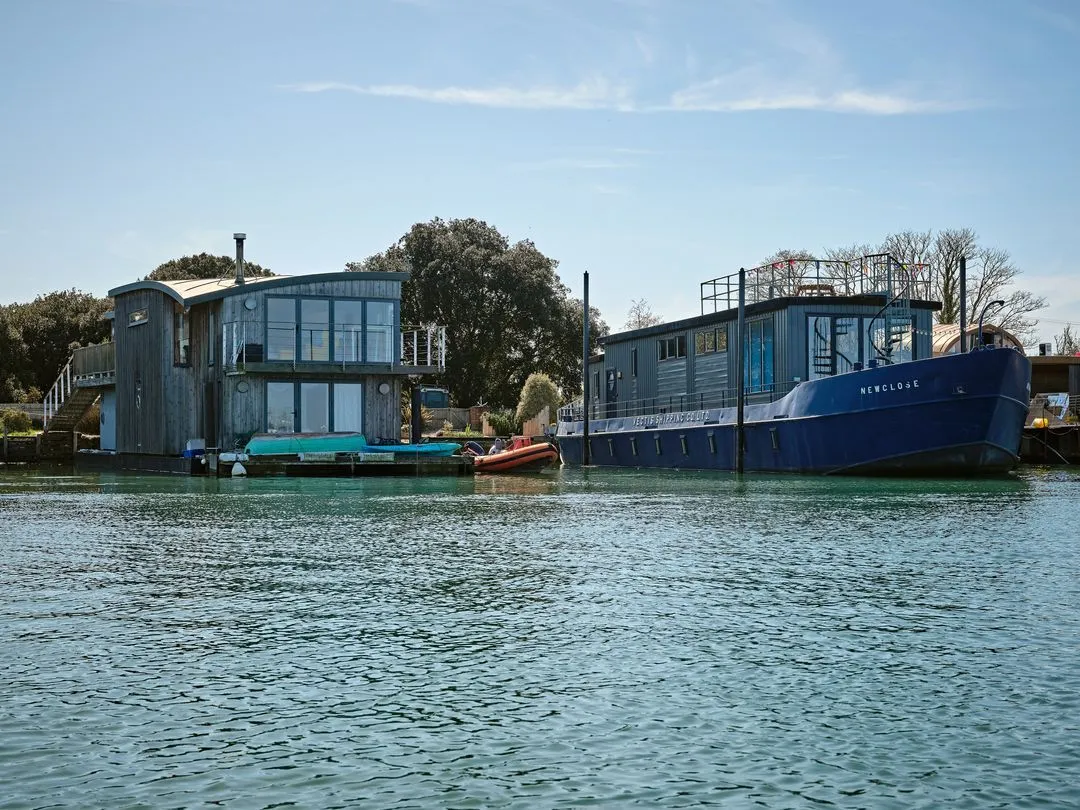 Two houseboats docked side by side on a calm river under a blue sky with trees in the background.