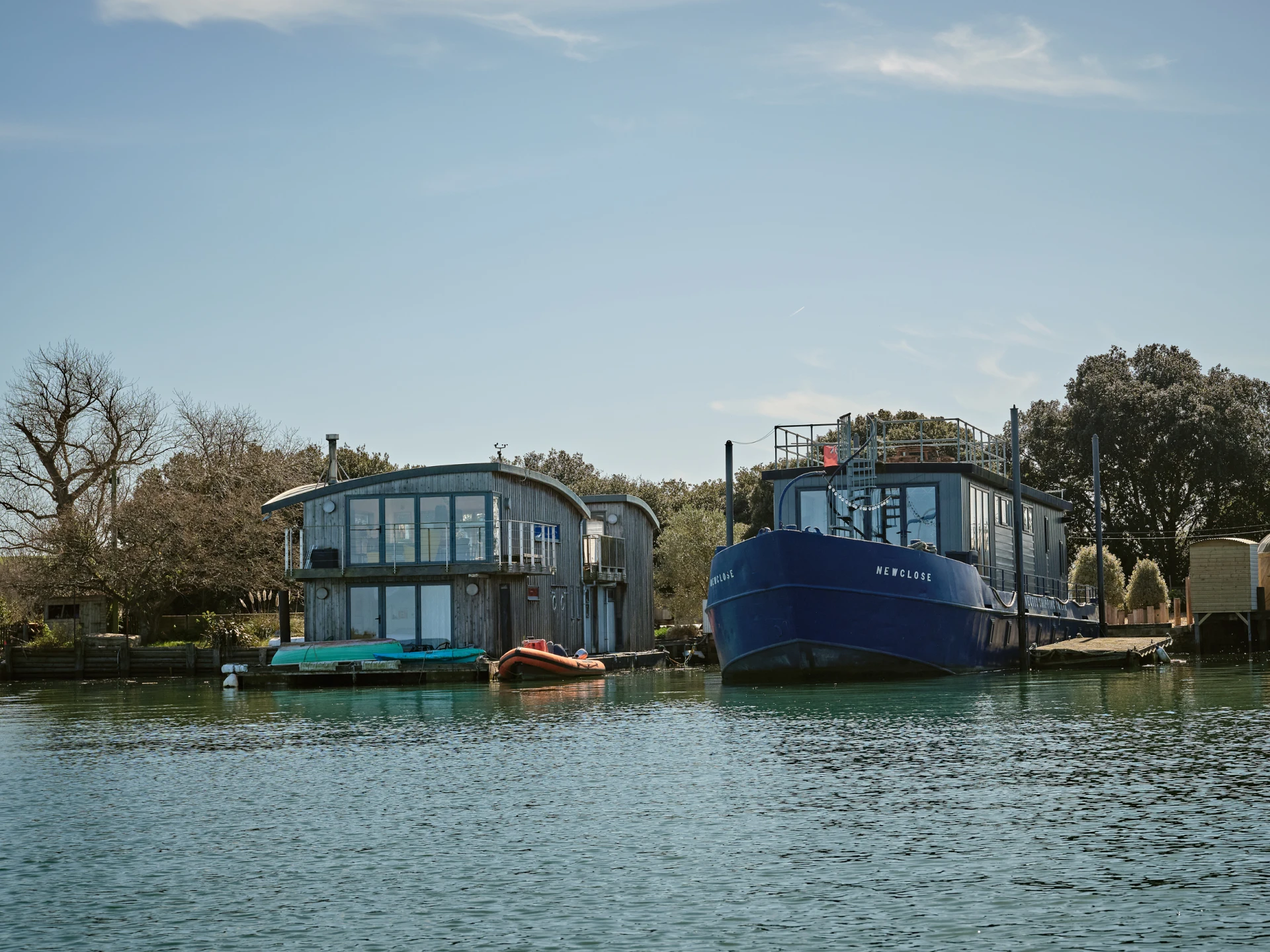 Woman in a scarf reading a book while sitting on a boat docked by a city canal with swans in the water.