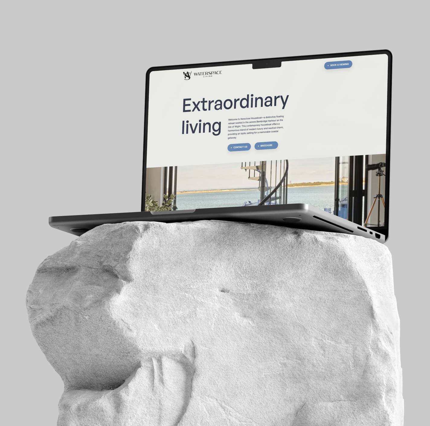 Laptop displaying a website titled 'Extraordinary living' with a coastal view background, placed on a large white rock.
