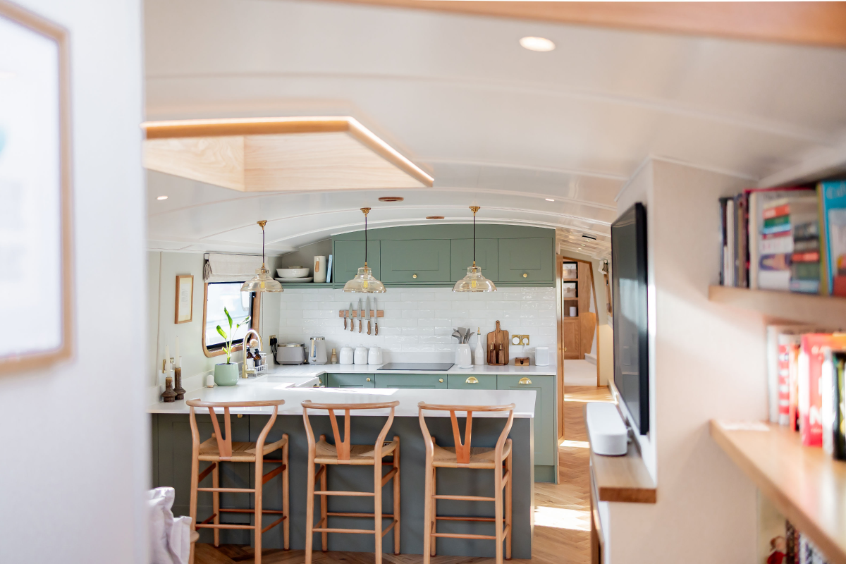 Black and gray narrowboat with orange trim docked in a canal near modern brick and concrete buildings.