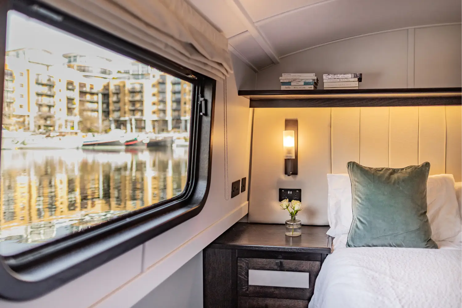 Cozy boat interior with a dining table set for four with wine glasses and a bottle, leather sofa, armchair, and windows showing water outside.