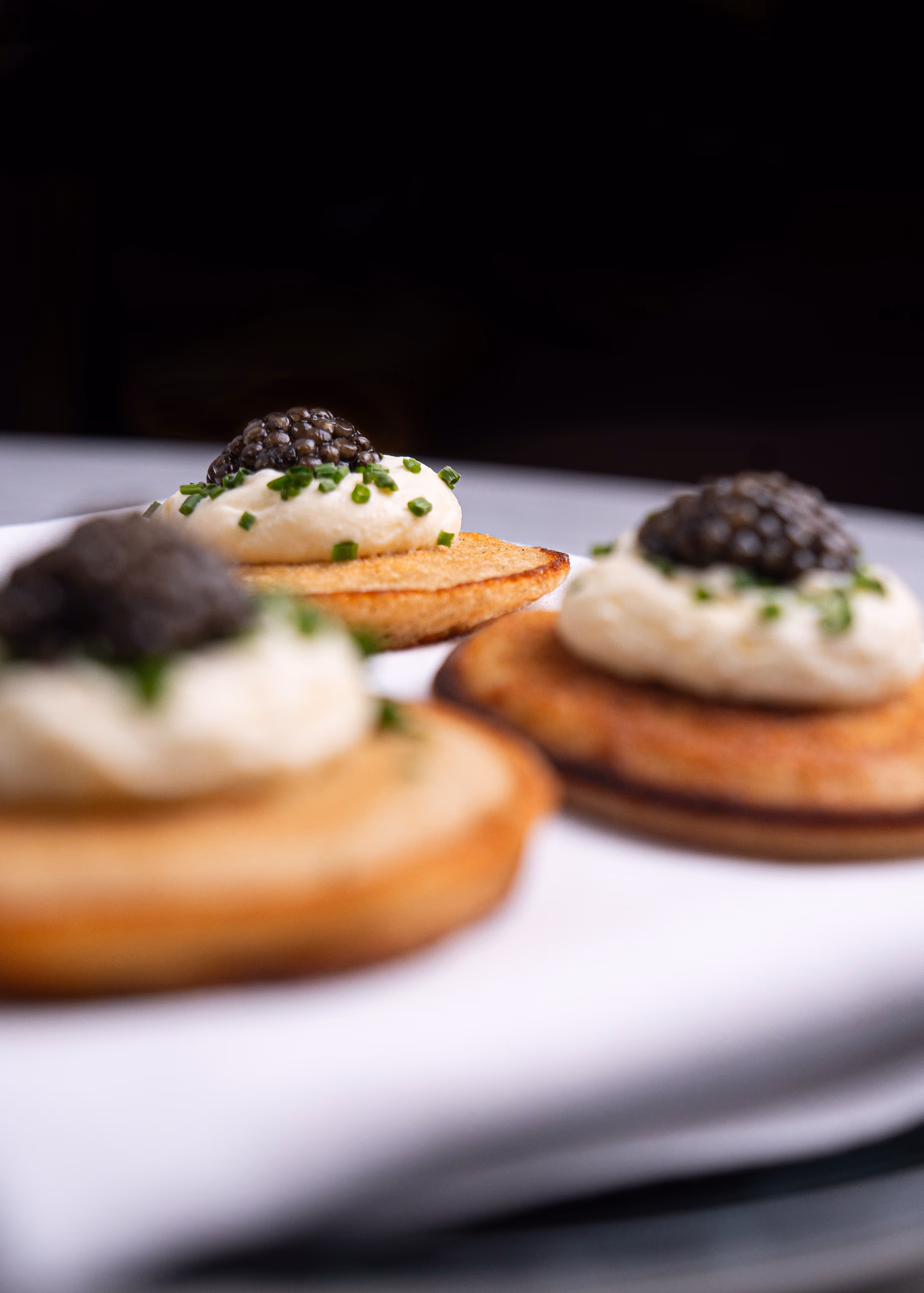 Close-up of three gourmet appetizers with cream, chives, and black caviar on toasted bread rounds.