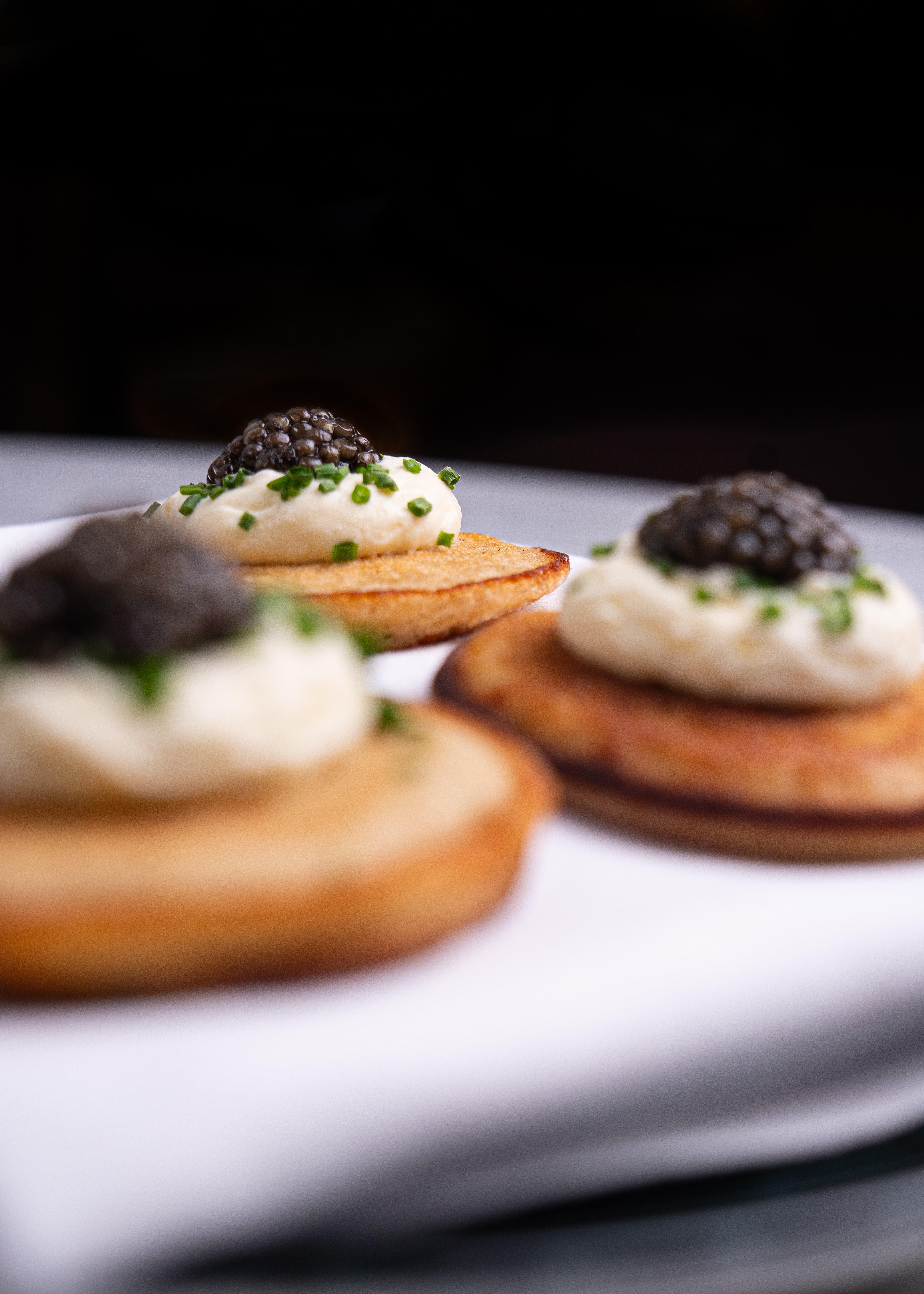 Close-up of three gourmet appetizers with cream, chives, and black caviar on toasted bread rounds.