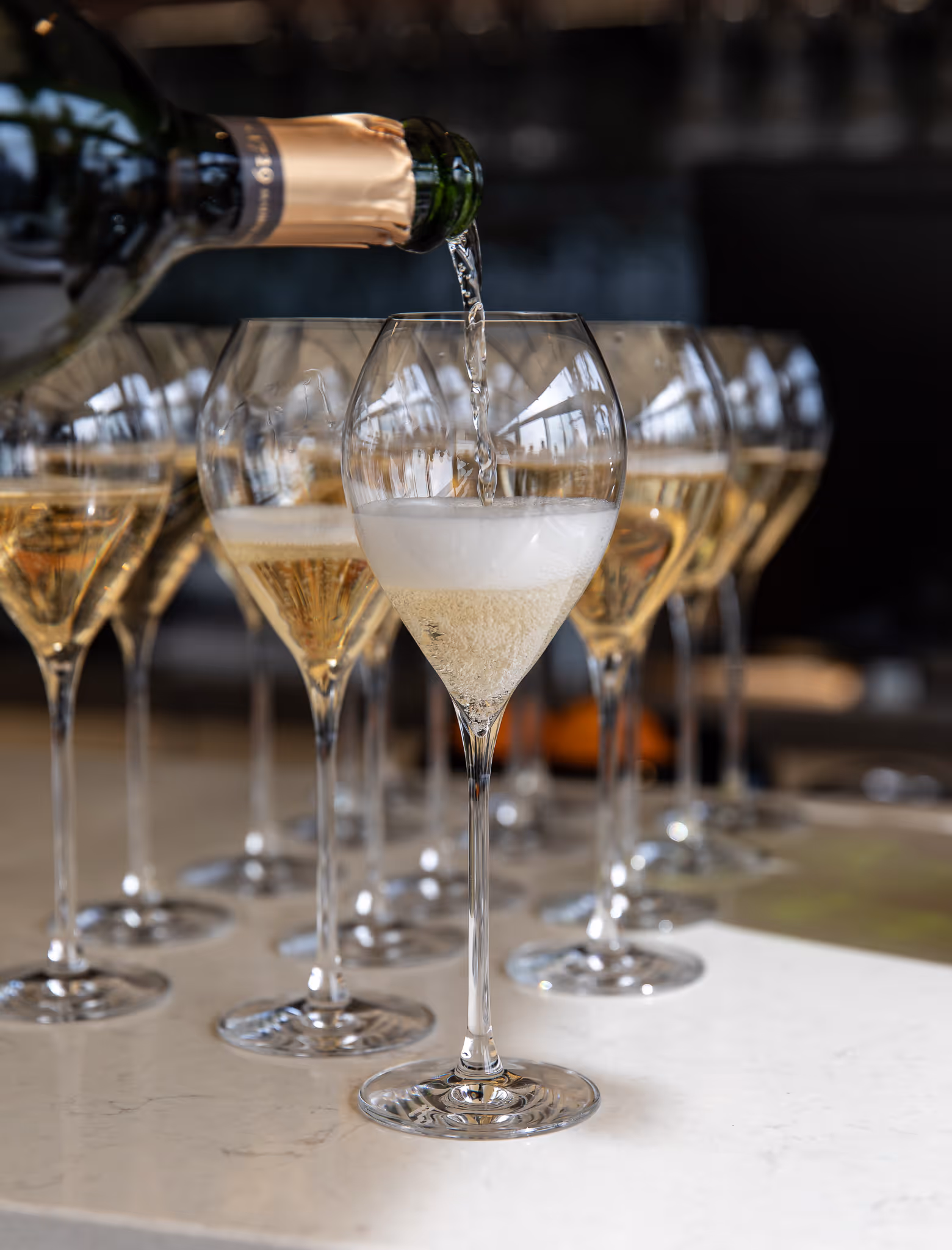 Hand with red nail polish sprinkling garnish onto a frothy iced cocktail topped with a nest of crispy noodles.