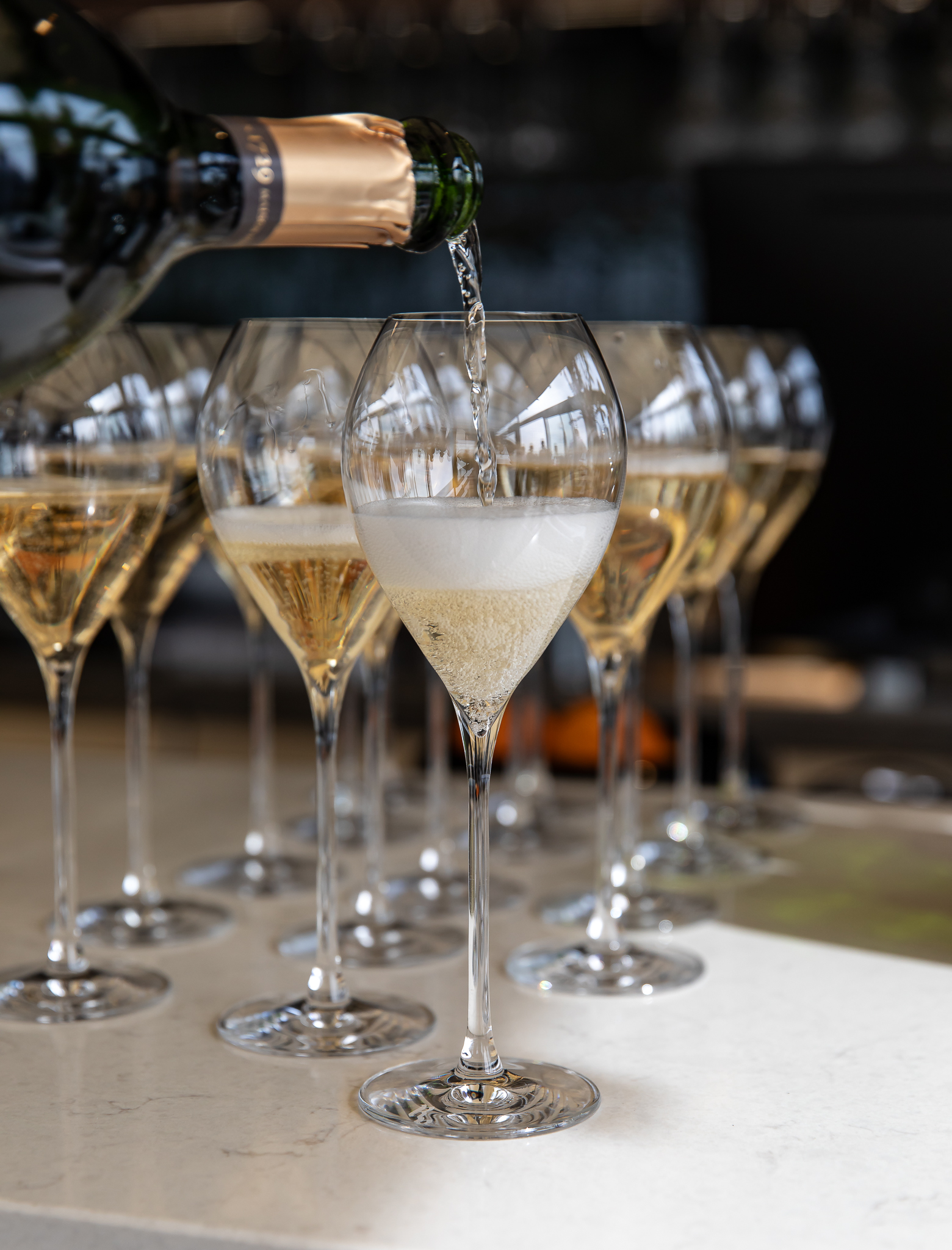 Hand with red nail polish sprinkling garnish onto a frothy iced cocktail topped with a nest of crispy noodles.