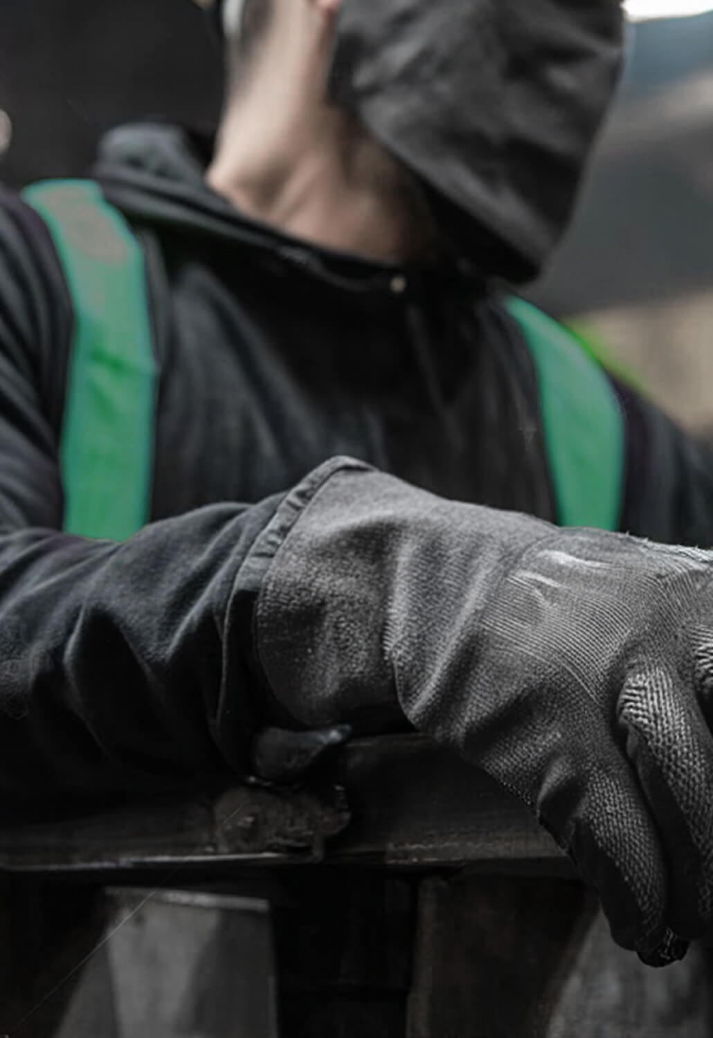 Worker wearing protective gloves and a hooded jacket in an industrial setting.