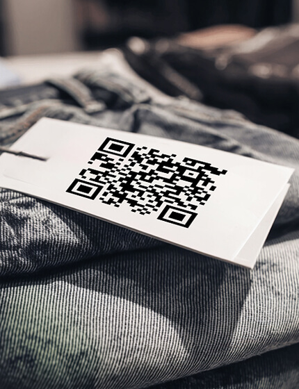 Close-up of a white clothing tag with a black QR code placed on folded denim fabric.
