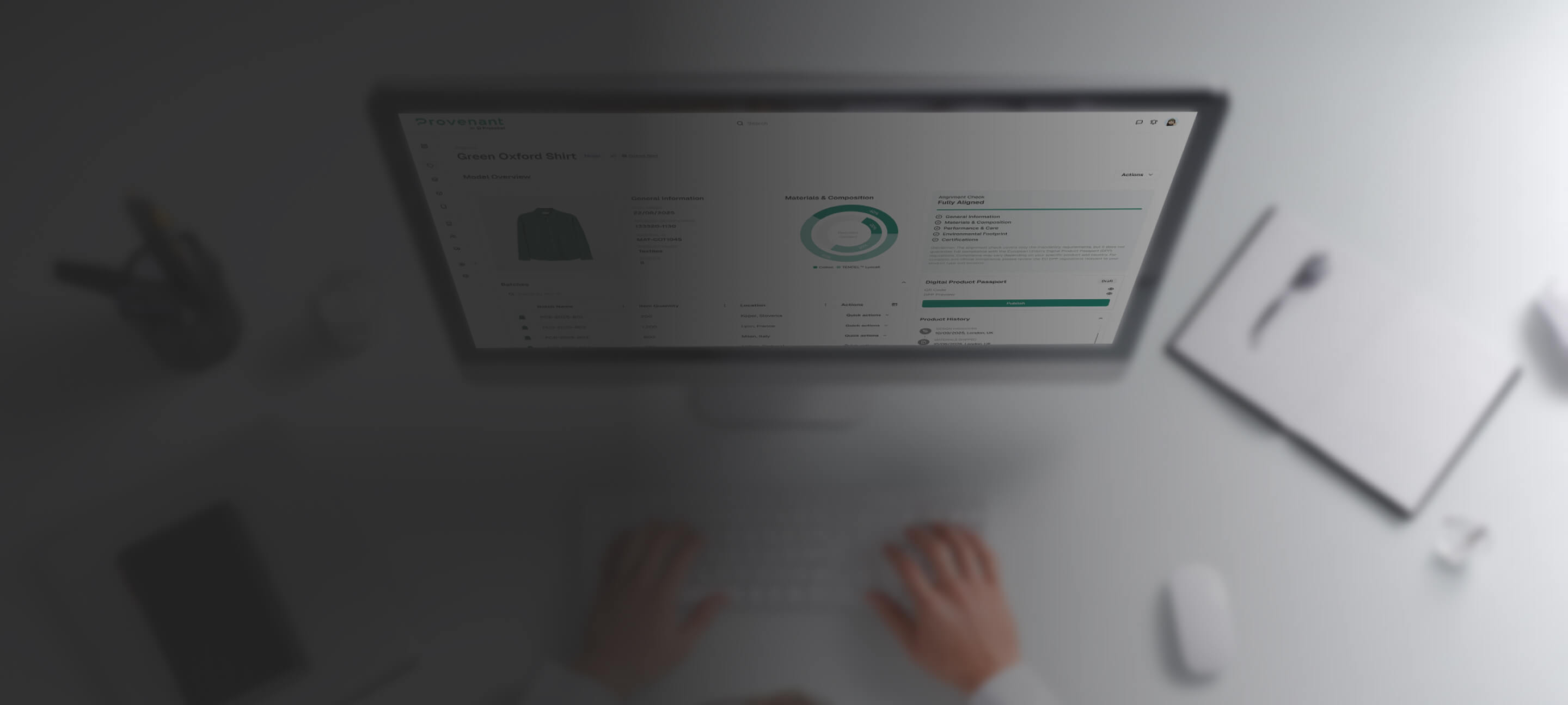 View from above of hands typing on a keyboard in front of a computer screen displaying a digital product overview for a green Oxford shirt.