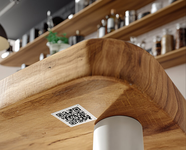 Close-up of a wooden furniture corner with a QR code sticker on it and blurred shelves with containers in the background.