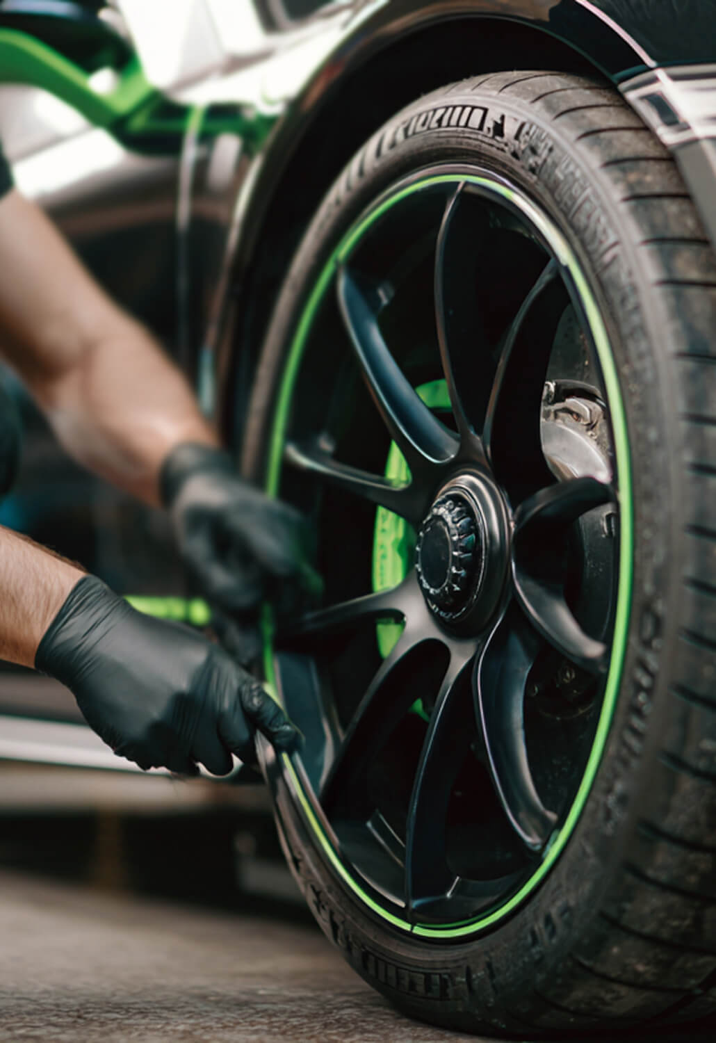 Person wearing black gloves working on a black car wheel with green rim accents.