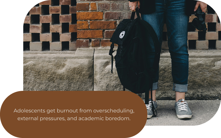 Image: A waist-down photo of a teenager wearing jeans and gray sneakers, holding their backpack in front of a brick wall. Text: Adolescents get burnout from. overscheduling, external pressures, and academic boredom. 