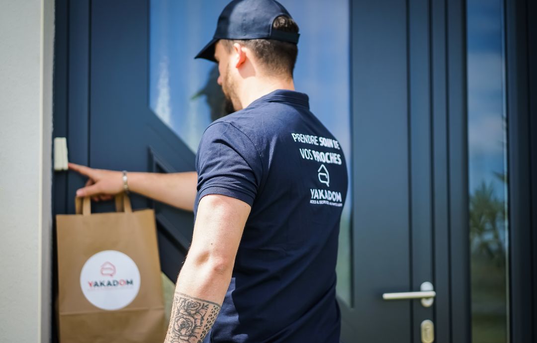 Livreur YAKADOM déposant un sac de courses devant la porte d’un domicile.