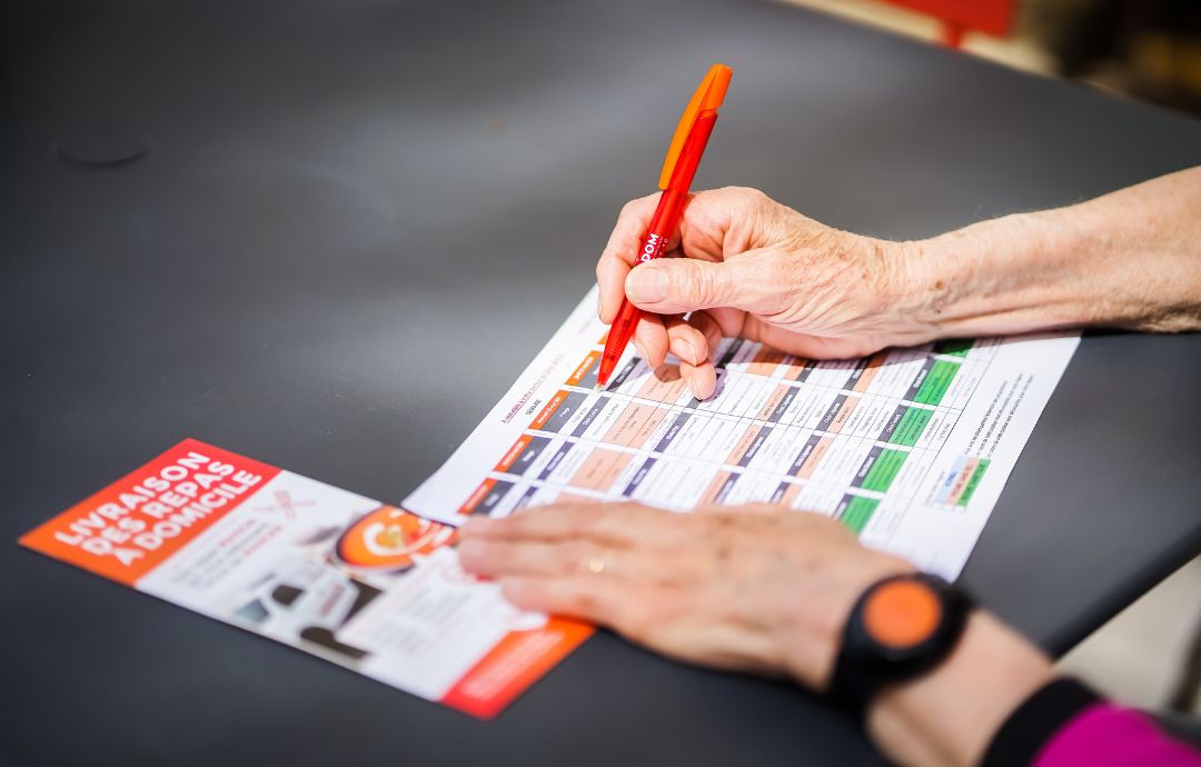 Main d’une personne remplissant un document d’organisation YAKADOM avec un stylo rouge.