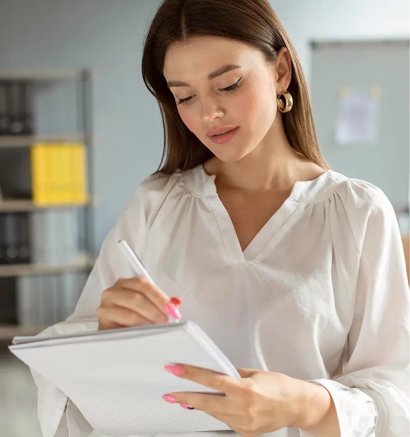 A woman in a white shirt is writing on a piece of paper.