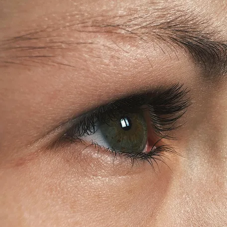 Close-up of a green eye with long eyelashes and detailed skin texture around it.