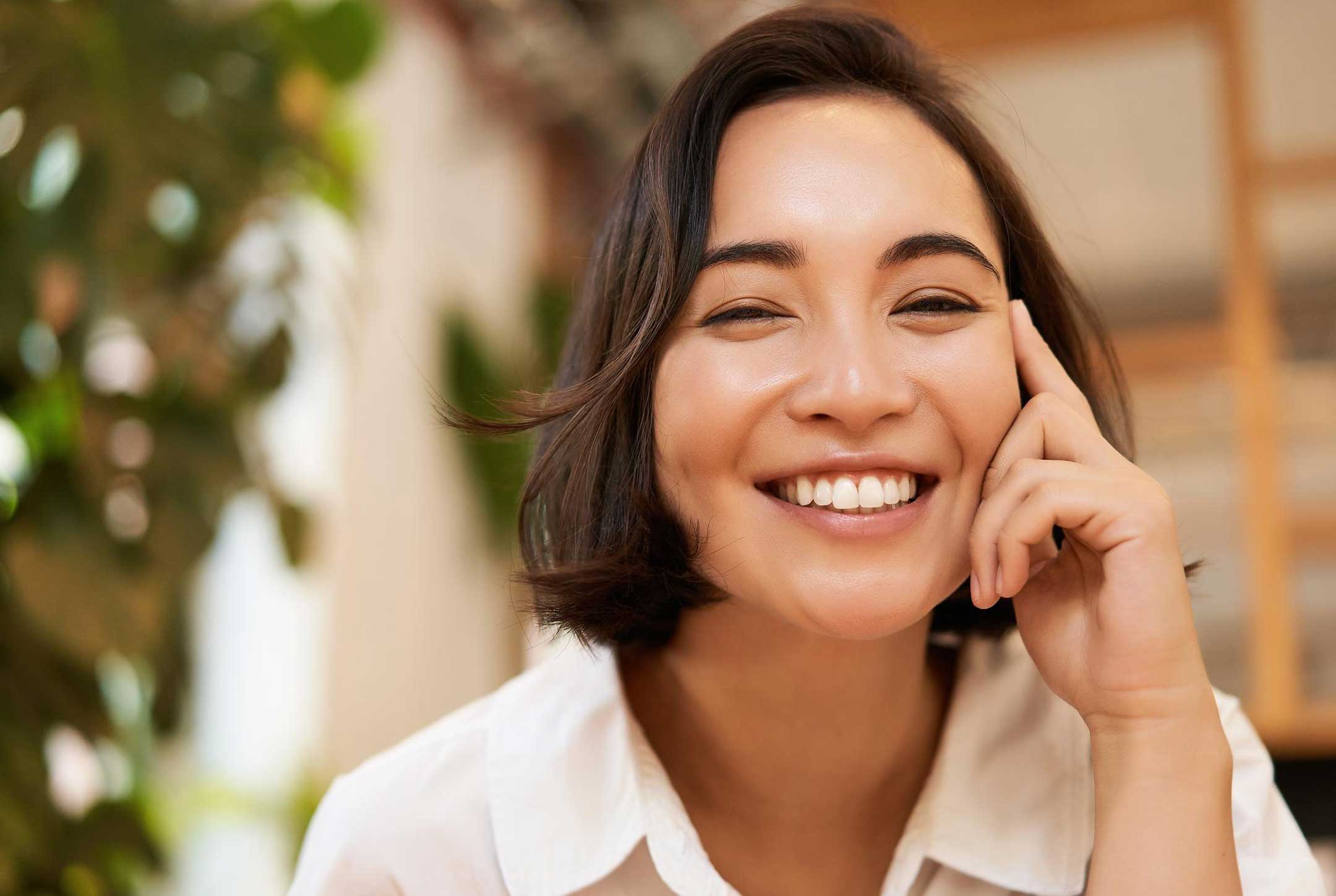 Close-up of a young woman with short dark hair smiling warmly indoors.