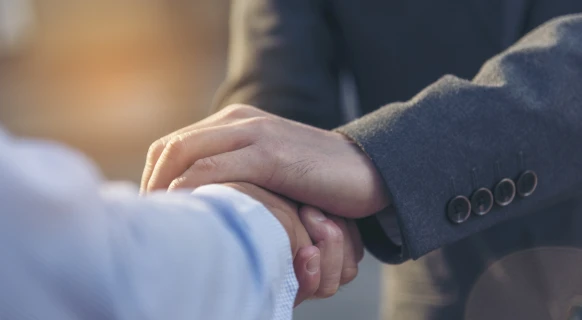 Two people shaking hands, one wearing a gray suit and the other a light blue shirt.