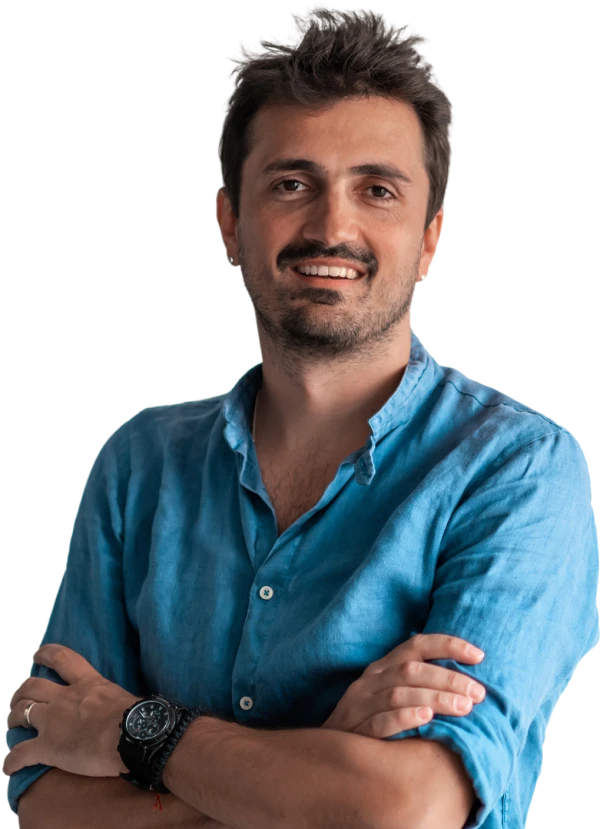 Smiling man with dark hair and a beard wearing a blue shirt with arms crossed.