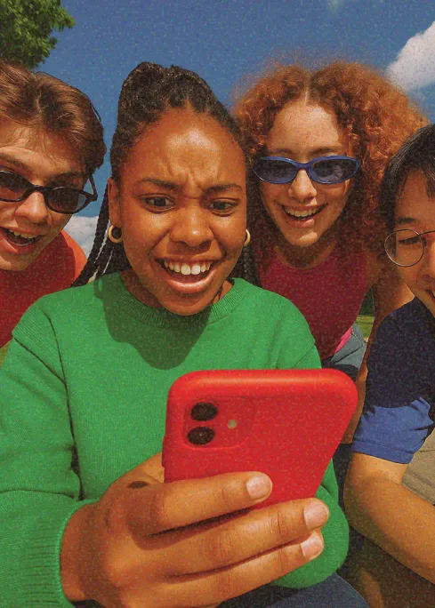 Group of friends smiling and reacting while looking at a red smartphone outdoors