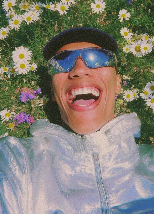 Person laughing in a field of daisies wearing reflective sunglasses and a silver jacket