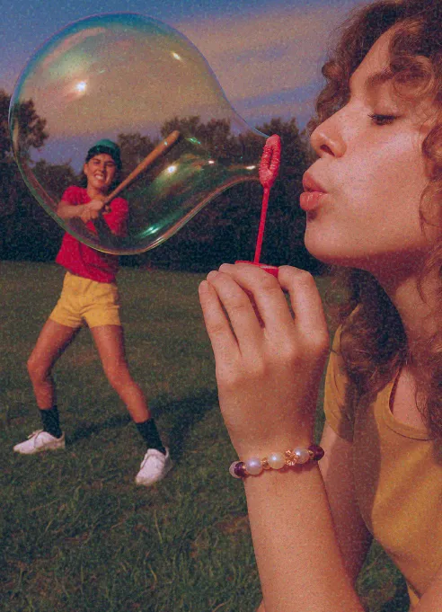 Person blowing a large soap bubble while another person swings a bat in the background