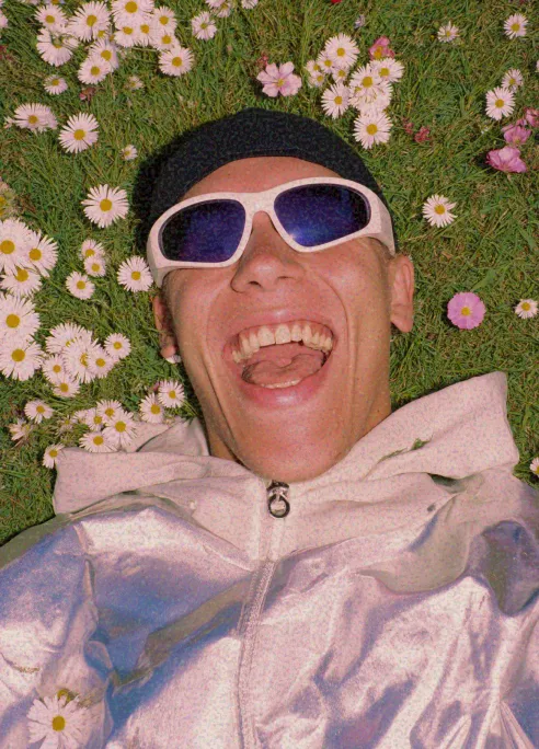 Person lying in a field of daisies laughing while wearing reflective sunglasses