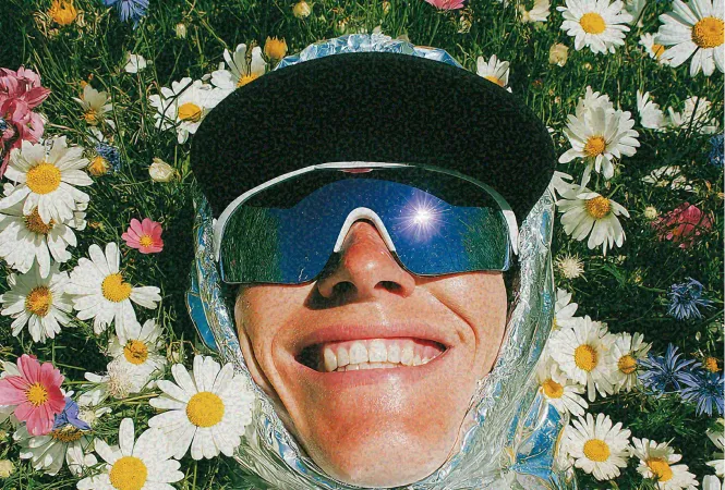 Person smiling in a field of daisies wearing reflective sunglasses and a cap