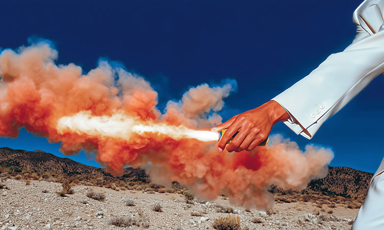 Person in a white suit releasing orange smoke in a desert landscape