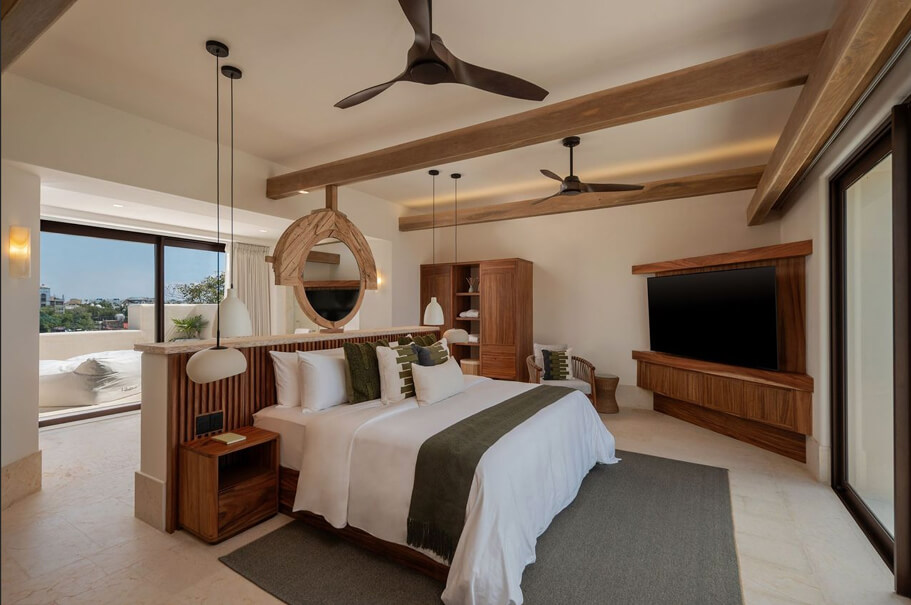 Dormitorio moderno con cama grande, ventiladores de techo, muebles de madera y una gran ventana que ofrece vista exterior.