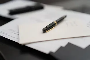 Zwarte pen met gouden accenten ligt op een witte envelop bovenop documenten op een donkere ondergrond.