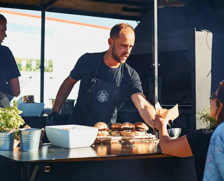 Verkoper geeft een papieren zak met hamburgers aan een klant bij een foodtruck.
