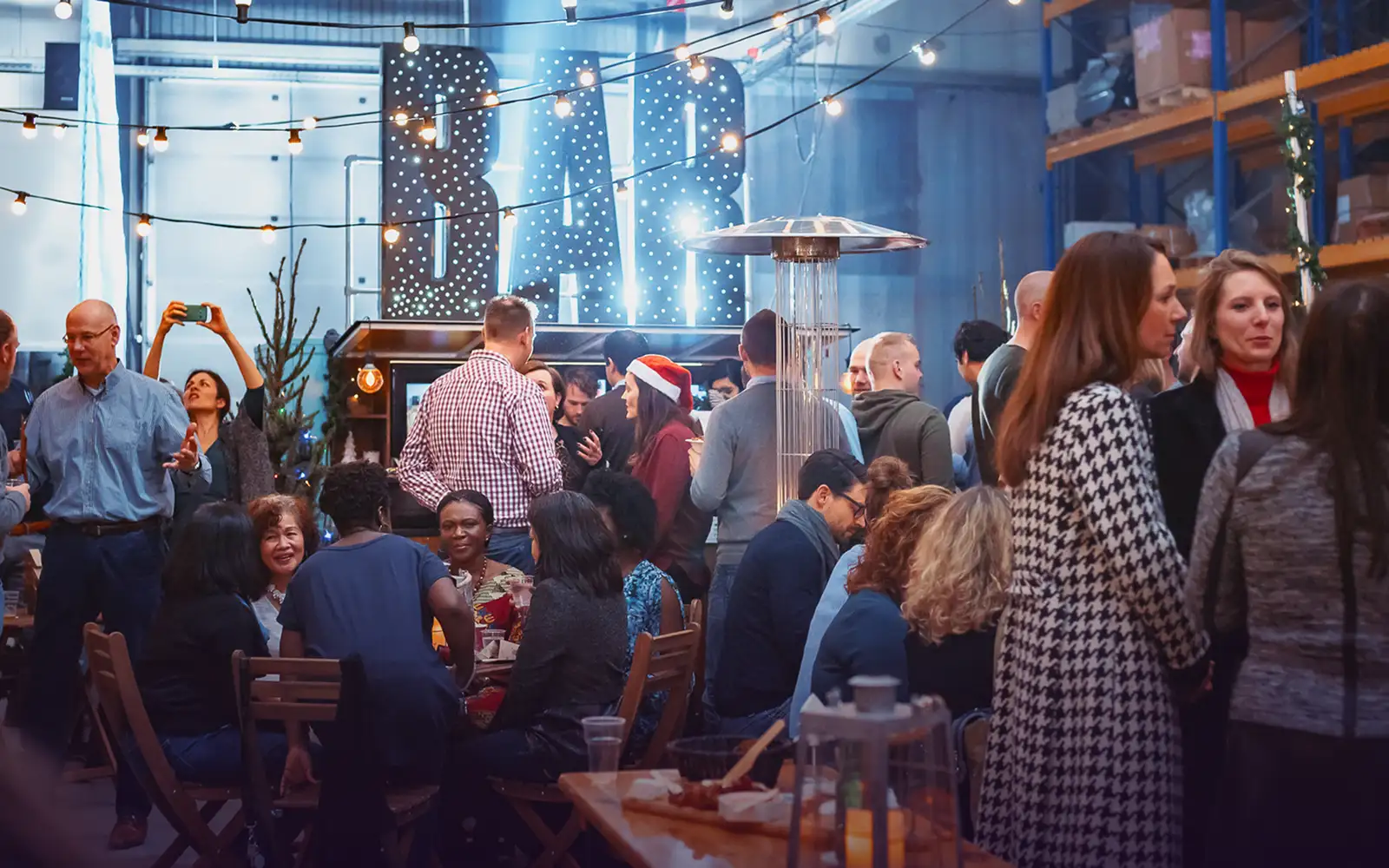 Mensen die genieten van een drukke barfeestgelegenheid met sfeerverlichting en een vrouw met een kerstmanmuts.