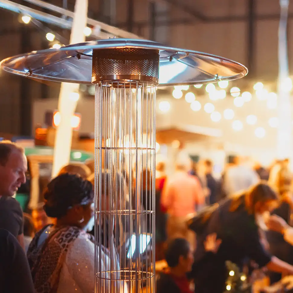 Buitenstaande terrasverwarmer met een groep mensen op de achtergrond bij een sfeervolle avondbijeenkomst.