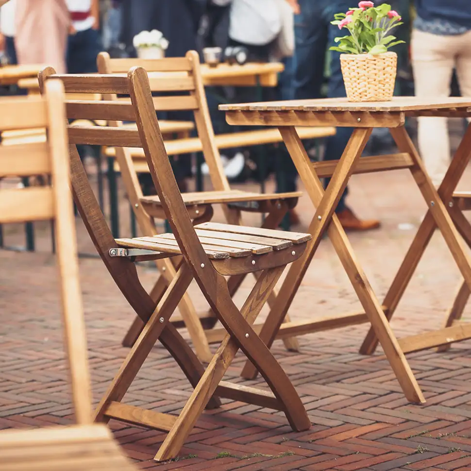 Houten plooistoelen en een tafel op een terras met een bloempot met planten erop.